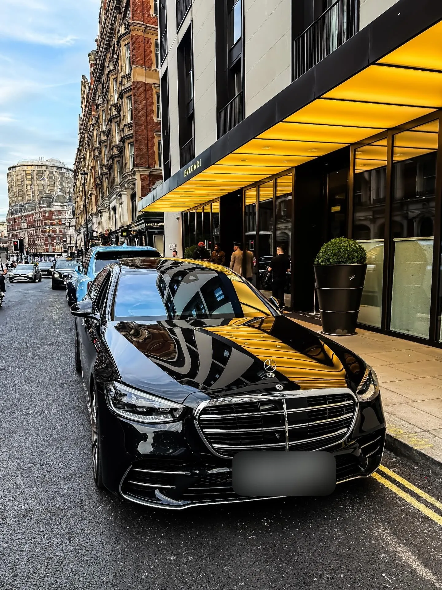 Polished black Mercedes S-Class at a London hotel entrance under a yellow canopy